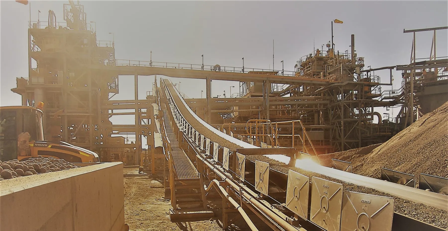 A processing plant conveyor carrying ore, with mill balls stockpiled alongside