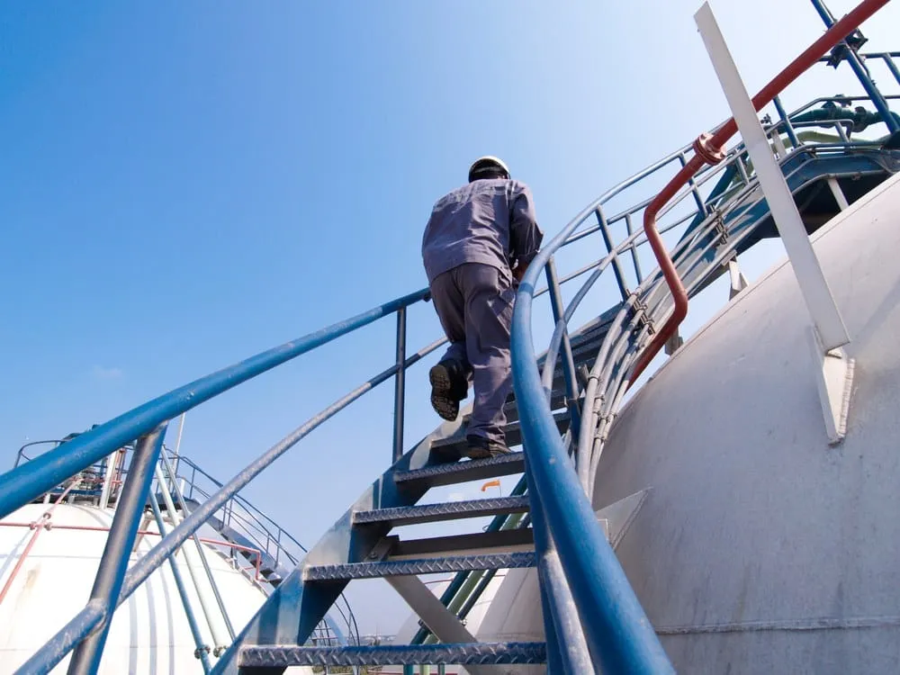 An operator climbing access stairs on a bulk storage tank farm